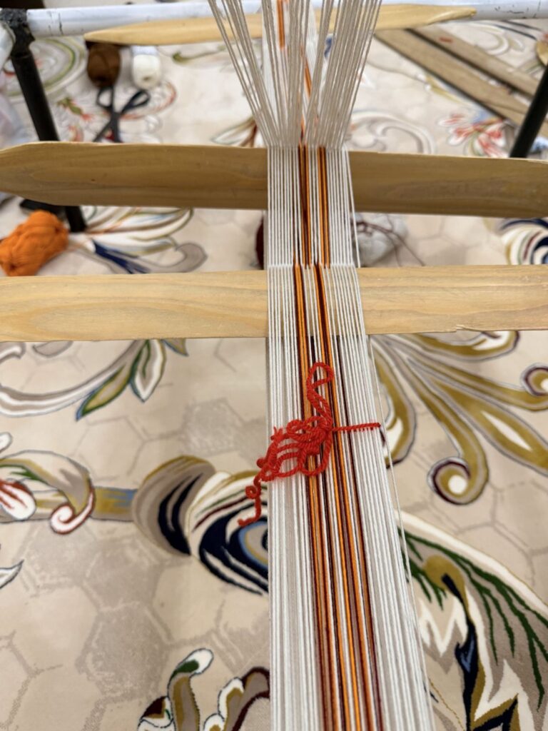 Sadu loom with striped warp threads tied with red thread