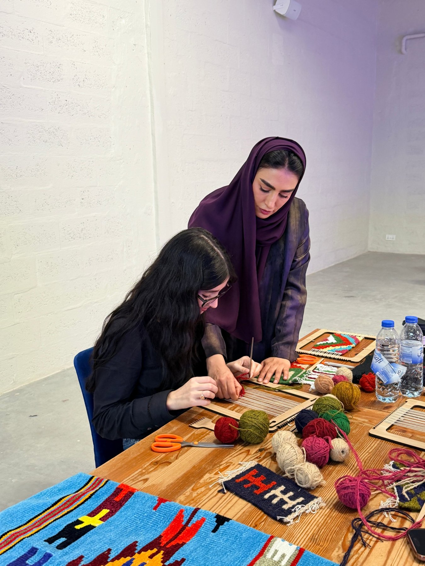 An Emirati artisan guiding a young weaver at the loom
