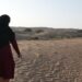Umm Saif walking across the dunes, pointing at tracks in the sand